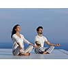 young couple practicing yoga at sunset in modern home terace with ocean and sunset in background