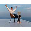 handsome young man relaxing and working on laptop computer at home balcony while looking sunset