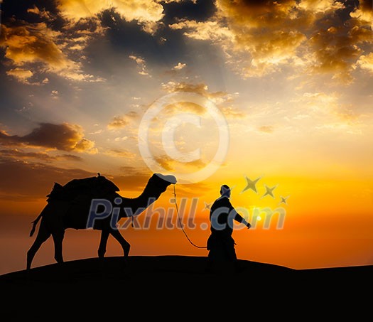 Rajasthan travel background - indian cameleer camel driver with camel silhouette in dunes of Thar desert on sunset. Jaisalmer, Rajasthan, India