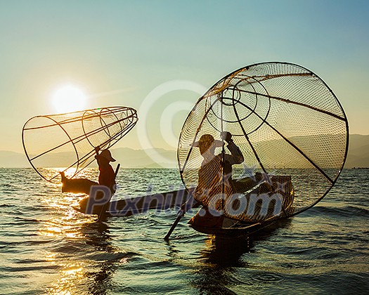 Myanmar travel attraction landmark - two traditional Burmese fishermen at Inle lake, Myanmar famous for their distinctive one legged rowing style on sunrise sunset Myanmar travel attraction landmark - two traditional Burmese fishermen at Inle lake, Myanmar famous for their distinctive one legged rowing style on sunrise sunset