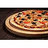 Ham pizza with capsicum and olives on wooden board on table close up