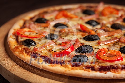 Ham pizza with capsicum and olives on wooden board on table close up