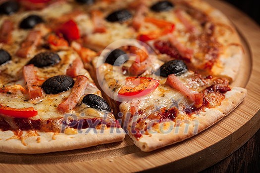 Sliced ham pizza with capsicum and olives on wooden board on table