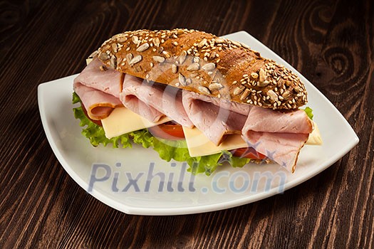 Ham sandwich with lettuce, cheese, tomato on plate on wooden table Ham sandwich with lettuce, cheese, tomato on plate on wooden table