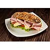 Ham sandwich with lettuce, cheese, tomato on plate on wooden table