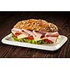 Ham sandwich with lettuce, cheese, tomato on plate on wooden table