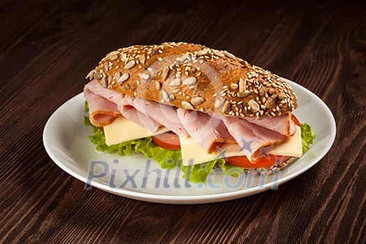 Ham sandwich with lettuce, cheese, tomato on plate on wooden table Ham sandwich with lettuce, cheese, tomato on plate on wooden table