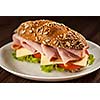 Ham sandwich with lettuce, cheese, tomato on plate on wooden table