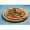 Ham pizza with capsicum, mushrooms, olives and basil leaves on wooden board on blue table