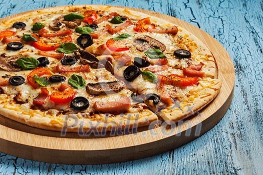 Ham pizza with capsicum, mushrooms, olives and basil leaves on wooden board on blue table Ham pizza with capsicum, mushrooms, olives and basil leaves on wooden board on blue table