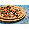 Ham pizza with capsicum, mushrooms, olives and basil leaves on wooden board on blue table