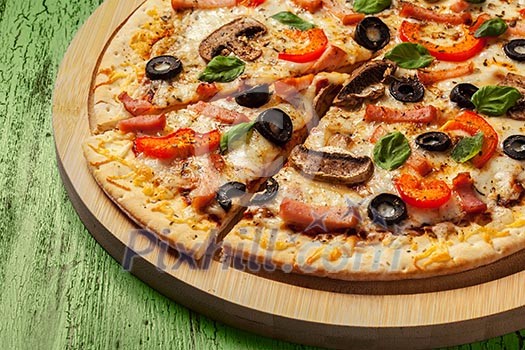 Ham pizza with capsicum, mushrooms, olives and basil leaves on wooden board on painted green table close up
