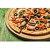Ham pizza with capsicum, mushrooms, olives and basil leaves on wooden board on painted green table close up