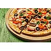 Ham pizza with capsicum, mushrooms, olives and basil leaves on wooden board on painted green table close up