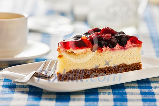 Dessert background - fruit cheese cake on plate with fork and coffee cup on blue checkered tablecloth