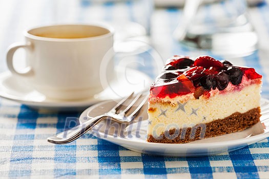 Dessert background - fruit cheese cake on plate with fork and coffee cup on blue checkered tablecloth