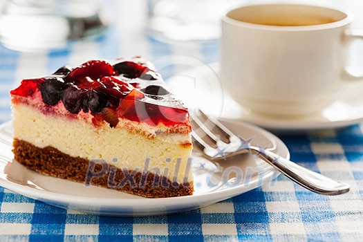 Dessert background - fruit cheese cake on plate with fork and coffee cup on blue checkered tablecloth