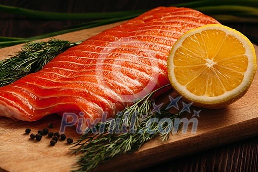 Fresh salmon piece on wooden cooking board with vegetables