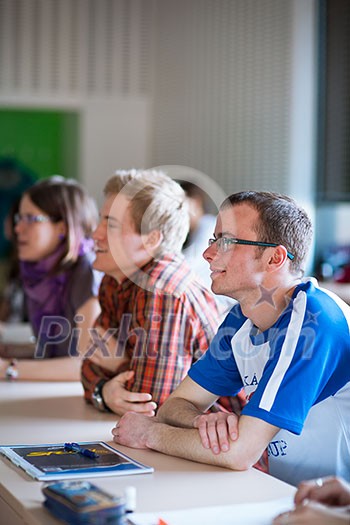 Handsome college student sitting in a classroom full of students during class  (color toned image; shallow DOF)