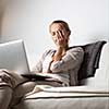 Very tired young woman, burning the midnigh oil - working late at night on her laptop computer, at home, sitting on sofa, rubbing her tired eyes, trying to stay focused