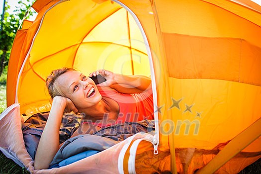 Pretty, young woman camping outdoors, lying in the tent in the morning, using her smart phone Pretty, young woman camping outdoors, lying in the tent in the morning, using her smart phone