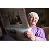 Senior woman reading morning newspaper, sitting in her favorite chair in her living room, looking happy