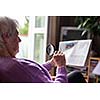 Senior woman reading morning newspaper, sitting in her favorite chair in her living room, looking happy