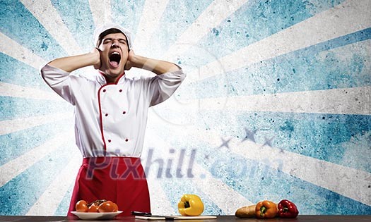 Young screaming cook and vegetables on table