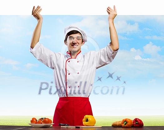 Young handsome cook holding white blank banner Young handsome cook holding white blank banner