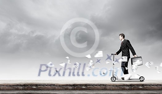 Young cheerful businessman riding scooter against city background Young cheerful businessman riding scooter against city background