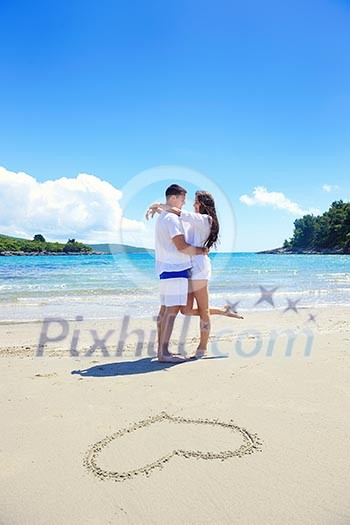 happy young couple have fun and relax on the summer with heart drawing on beach sand happy young couple have fun and relax on the summer with heart drawing on beach sand