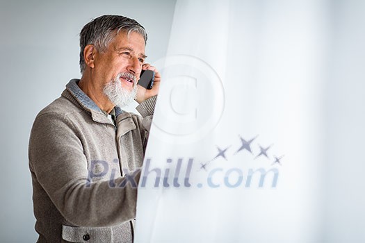 Handsome senior man calling on his cell phone and looking from a window at his house (shallow DOF; color toned image)
