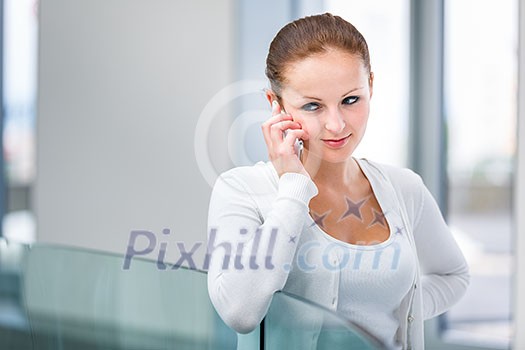Pretty, young woman calling on her call phone, pensive, concentrating, wearing bright clothes inside a modern, fresh interior (color toned image; shallow DOF)