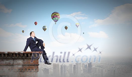 Young businessman sitting on roof of building Young businessman sitting on roof of building