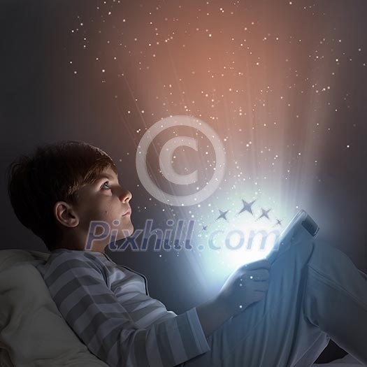 Little cute boy sitting in bed and using tablet