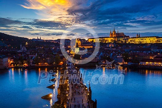 Aerial view of illuminated Prague castle and Charles Bridge with tourist crowd over Vltava river in Prague, Czech Republic. Prague, Czech Republic in the evening Aerial view of illuminated Prague castle and Charles Bridge with tourist crowd over Vltava river in Prague, Czech Republic. Prague, Czech Republic in the evening