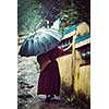 Vintage retro effect filtered hipster style image of  Buddhist monk with umbrella spinning prayer wheels on kora around Tsuglagkhang complex in McLeod Ganj, Himachal Pradesh, India. 