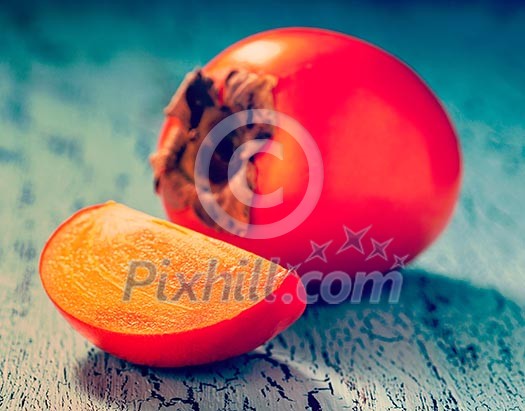 Vintage retro effect filtered hipster style image of fresh ripe persimmon with slice on a blue wooden background