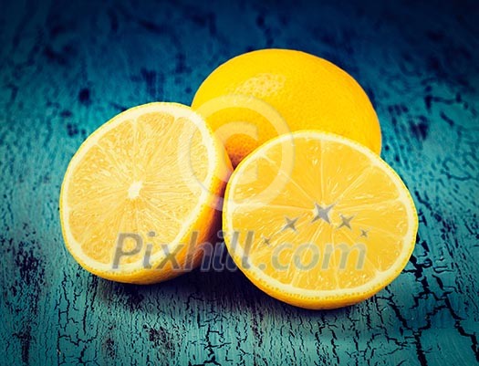 Vintage retro effect filtered hipster style image of lemon and cut half slice on blue wooden background Vintage retro effect filtered hipster style image of lemon and cut half slice on blue wooden background