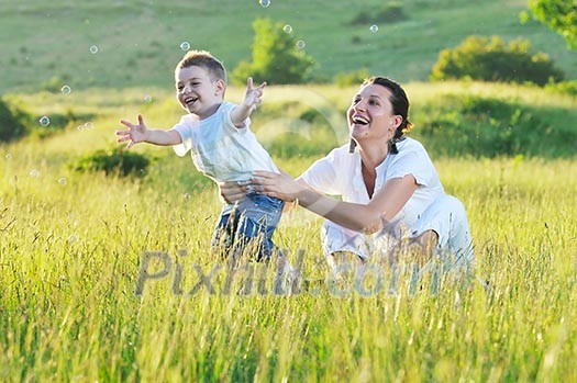 happy child and woman outdoor playing with soap bubble on meadow