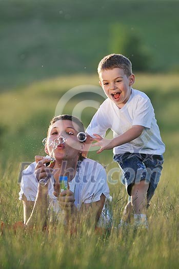 happy child and woman outdoor playing with soap bubble on meadow