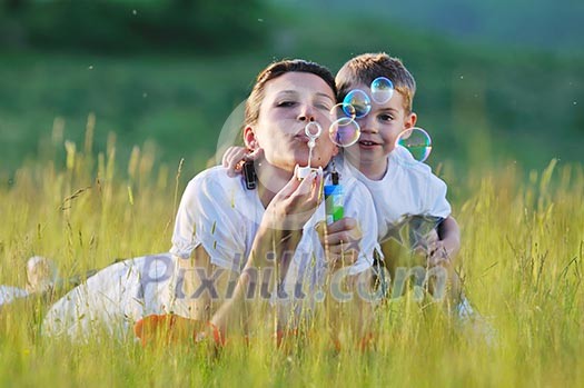 happy child and woman outdoor playing with soap bubble on meadow