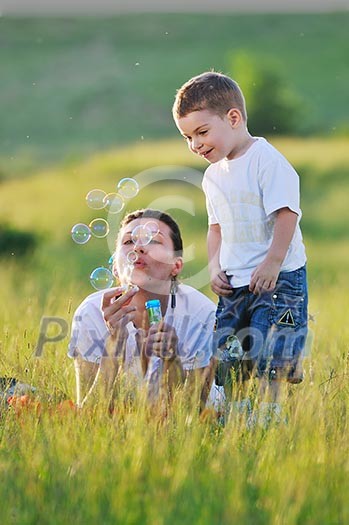 happy child and woman outdoor playing with soap bubble on meadow