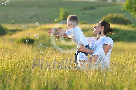 happy child and woman outdoor playing with soap bubble on meadow