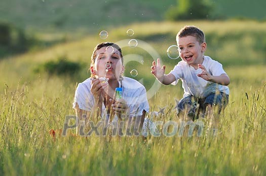 happy child and woman outdoor playing with soap bubble on meadow