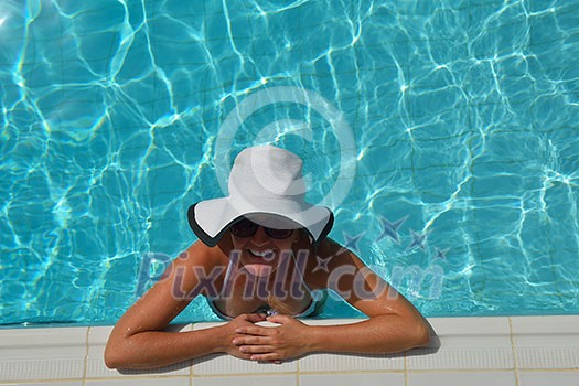 Happy smiling woman with hat and sunglasses  in swimming pool at tropical resort