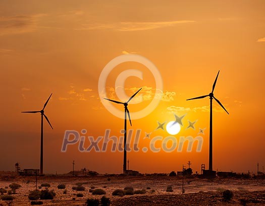 Green renewable energy concept - wind generator turbines sihouettes on sunset