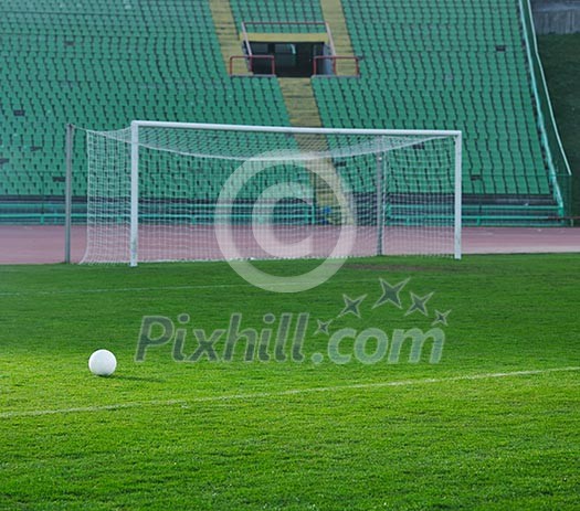 white Soccer ball on grass at goal and stadium in background white Soccer ball on grass at goal and stadium in background