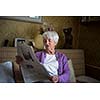 Senior woman reading morning newspaper, sitting in her favorite chair in her living room, looking happy