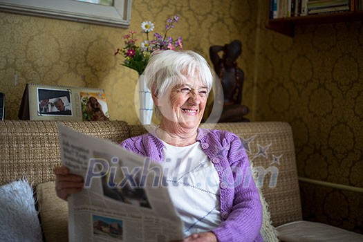Senior woman reading morning newspaper, sitting in her favorite chair in her living room, looking happy Senior woman reading morning newspaper, sitting in her favorite chair in her living room, looking happy
